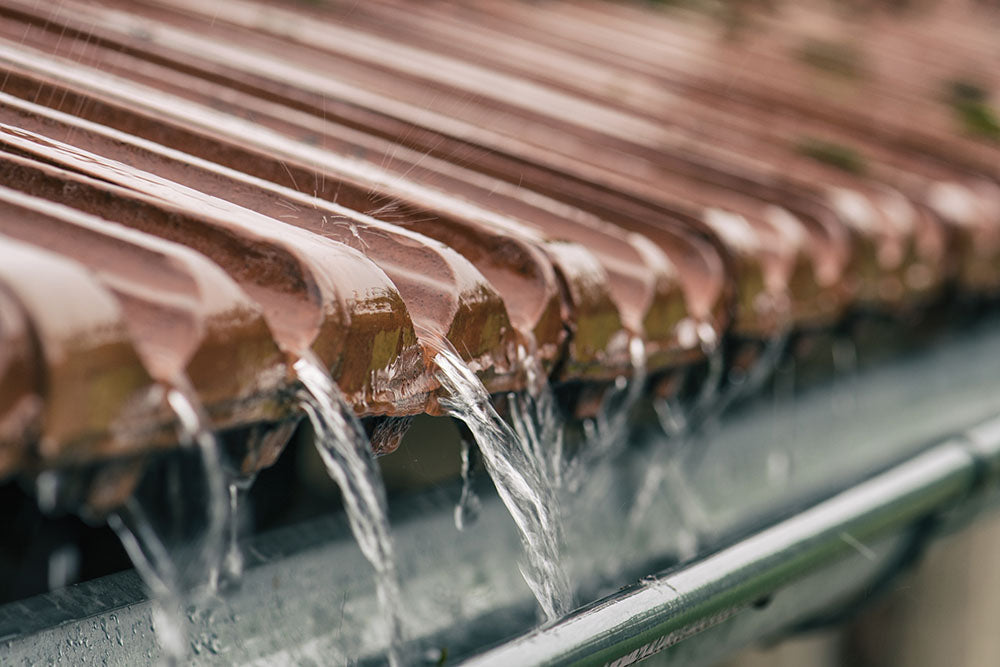 Rainwater dripping off a ridged roof and collecting in a metal gutter. 