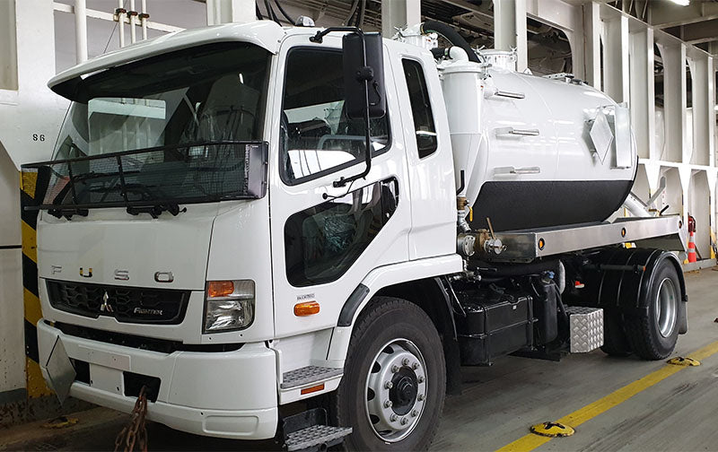 A white truck with a tanker on the back parked next to a white building. 